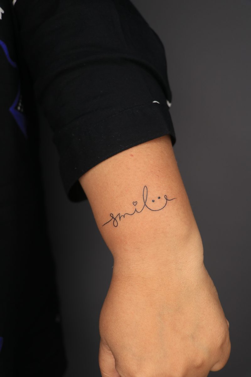 Smile script with smiley fine line wrist tattoo