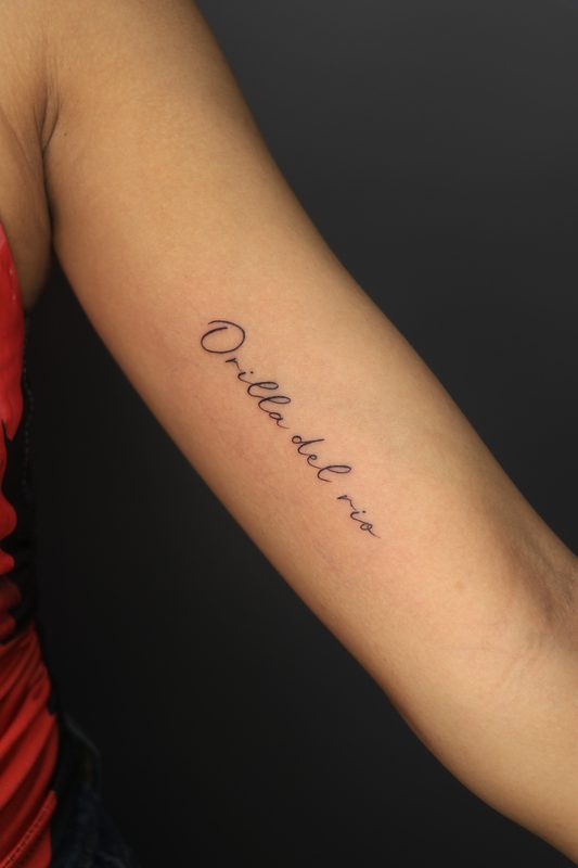 Orilla del rio cursive script tattoo on inner arm